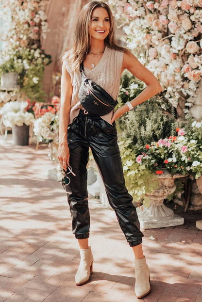 Woman in stylish outfit with leather pants and beige boots standing in front of floral decorations.