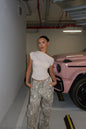 Woman in a white top and camouflage pants standing in a garage with a pink car.