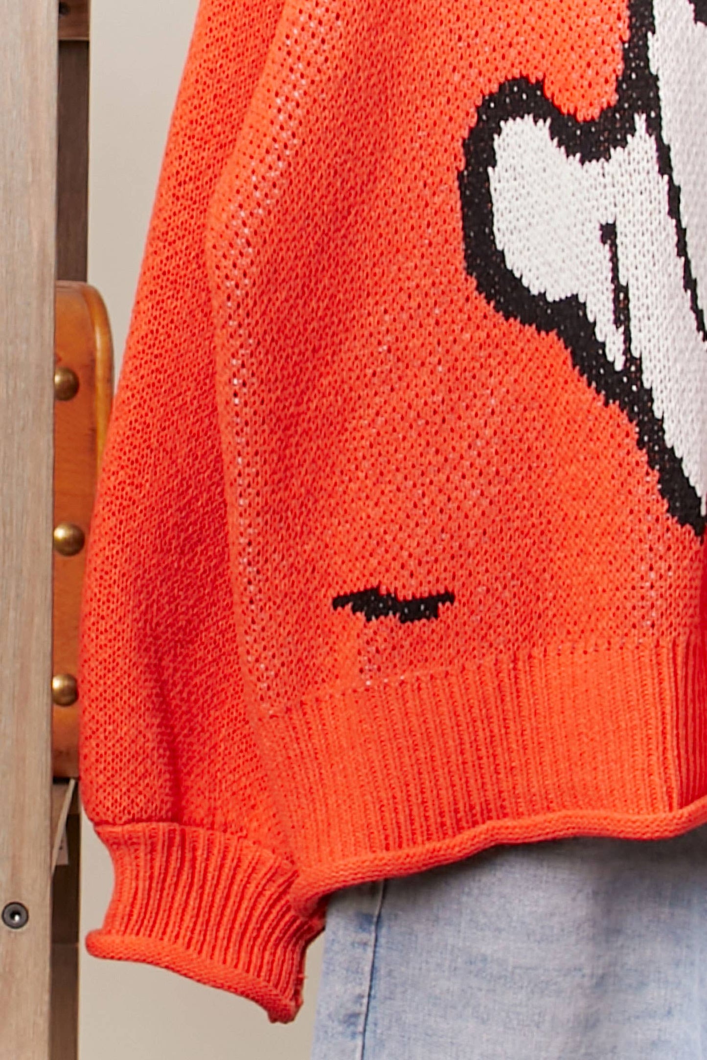 Close-up of an orange sweater with a graphic design on a wooden chair.