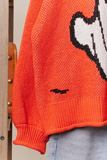 Close-up of an orange sweater with a graphic design on a wooden chair.