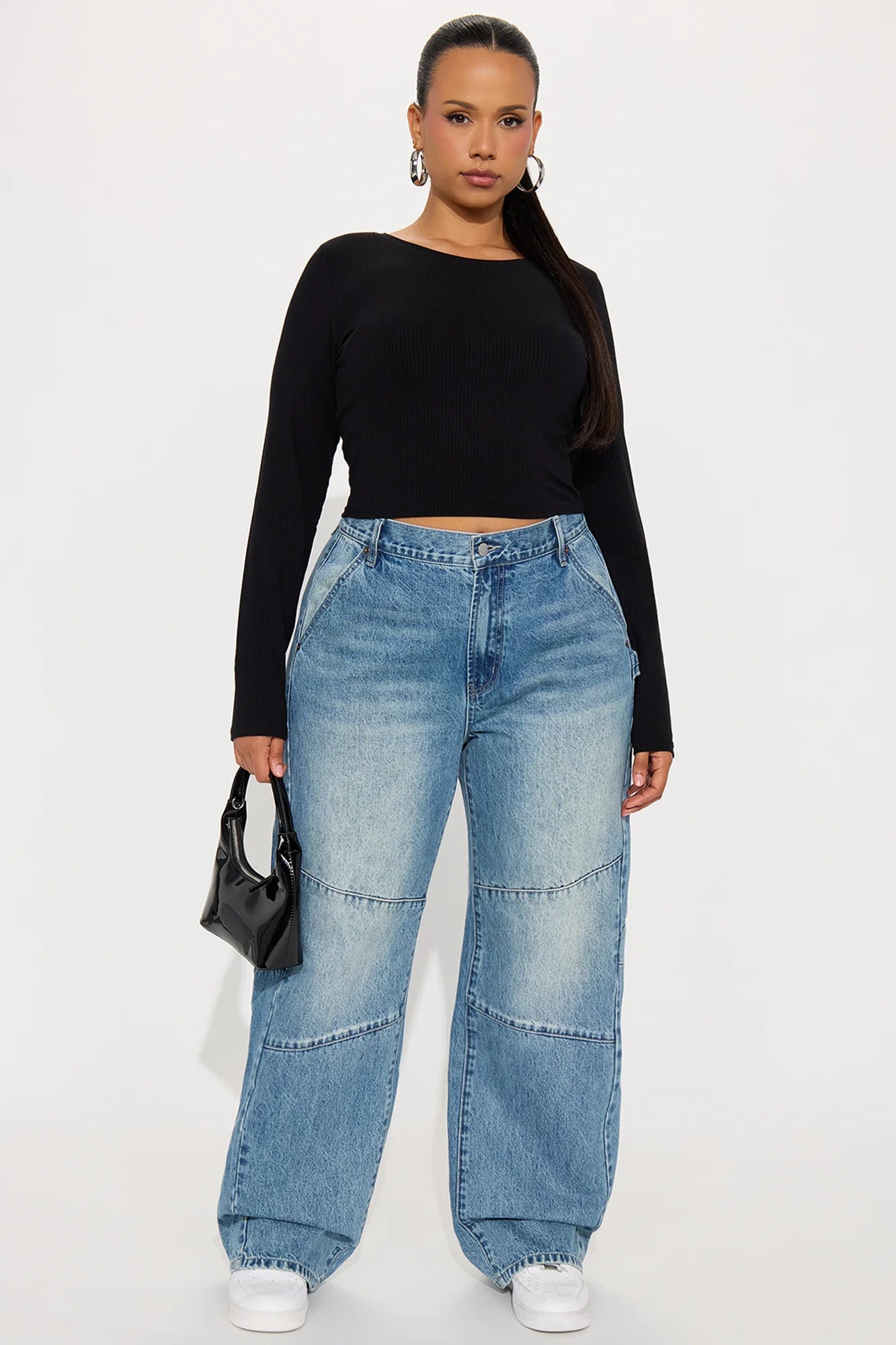 Woman wearing a black long-sleeve top and blue jeans on a white background