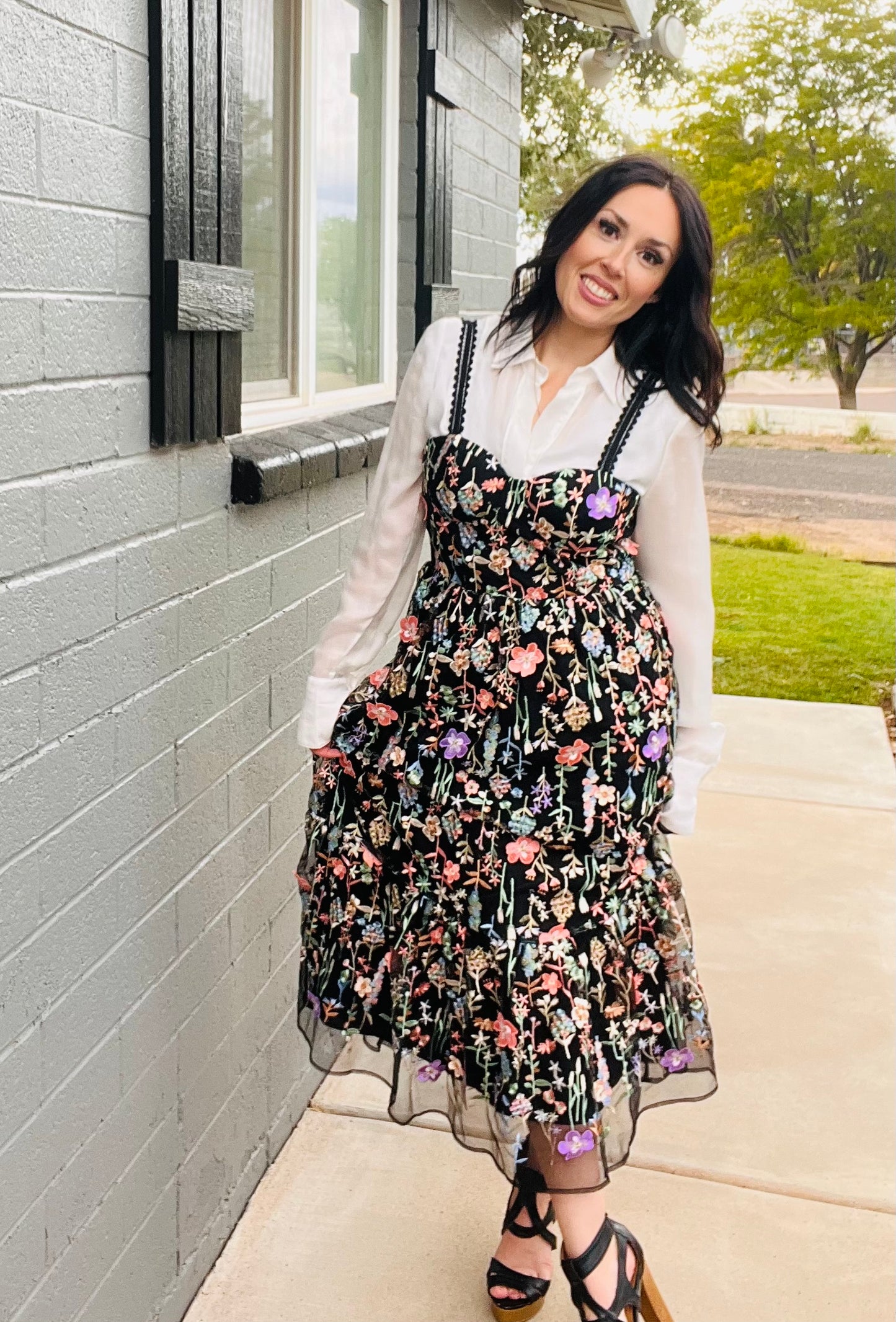 Woman wearing a floral dress and white shirt standing outside a building.