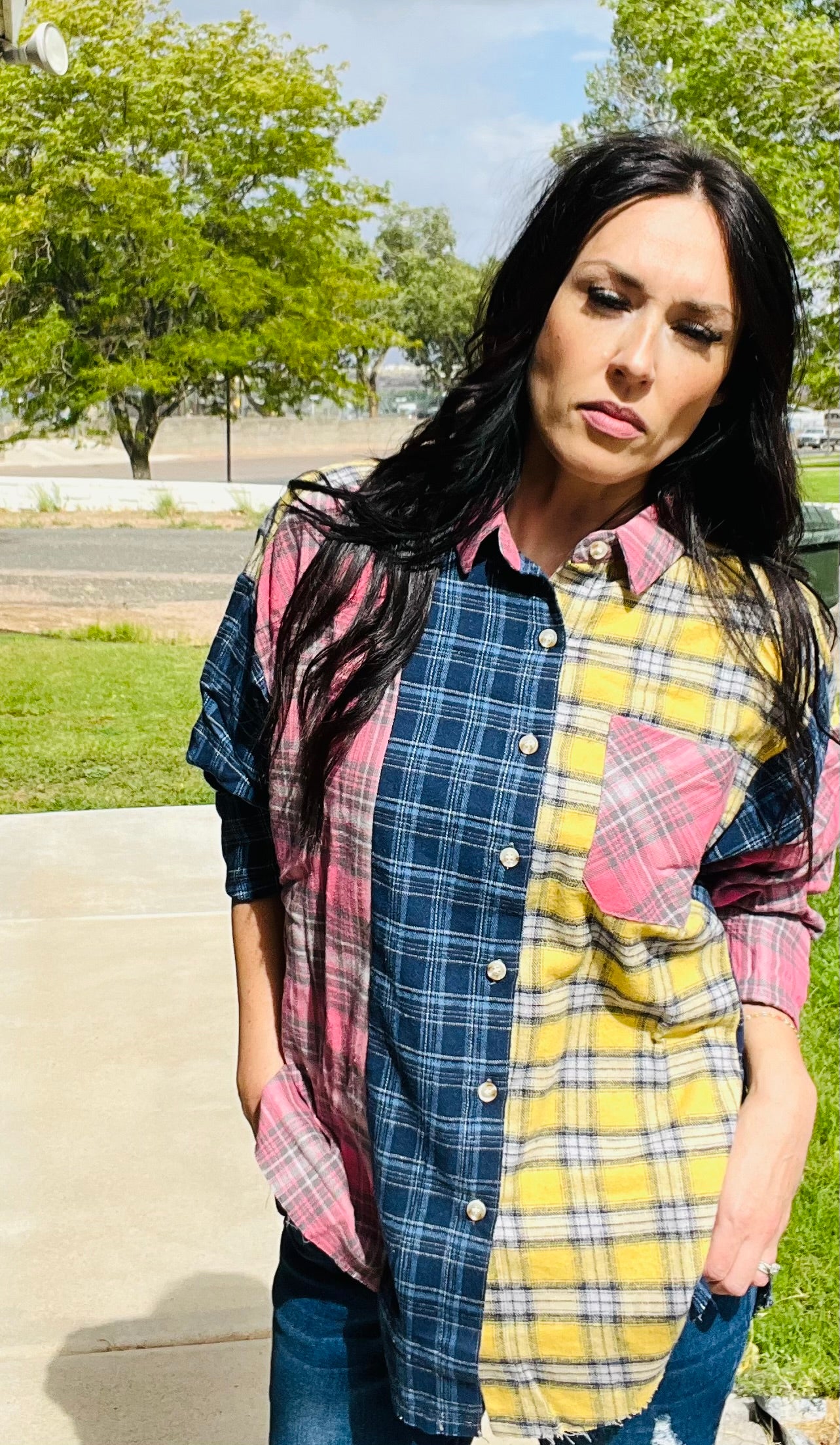 Woman wearing a patchwork plaid shirt outdoors with trees and grass in the background