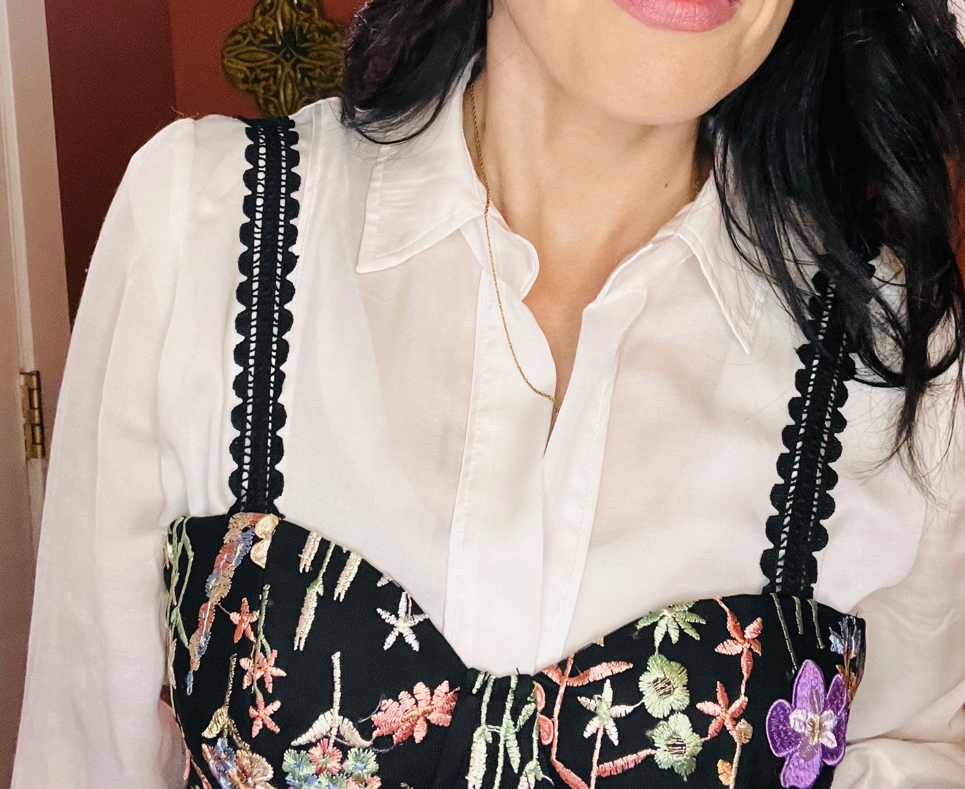 Person wearing a white blouse with floral embroidery on black straps.