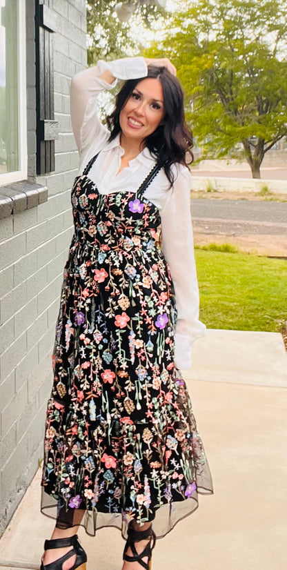 Woman wearing a floral dress with a white shirt and black high-heeled shoes outdoors.
