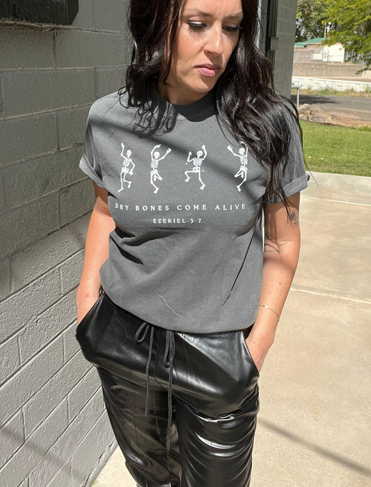 Person wearing a gray t-shirt with graphic design and text, standing against a brick wall.