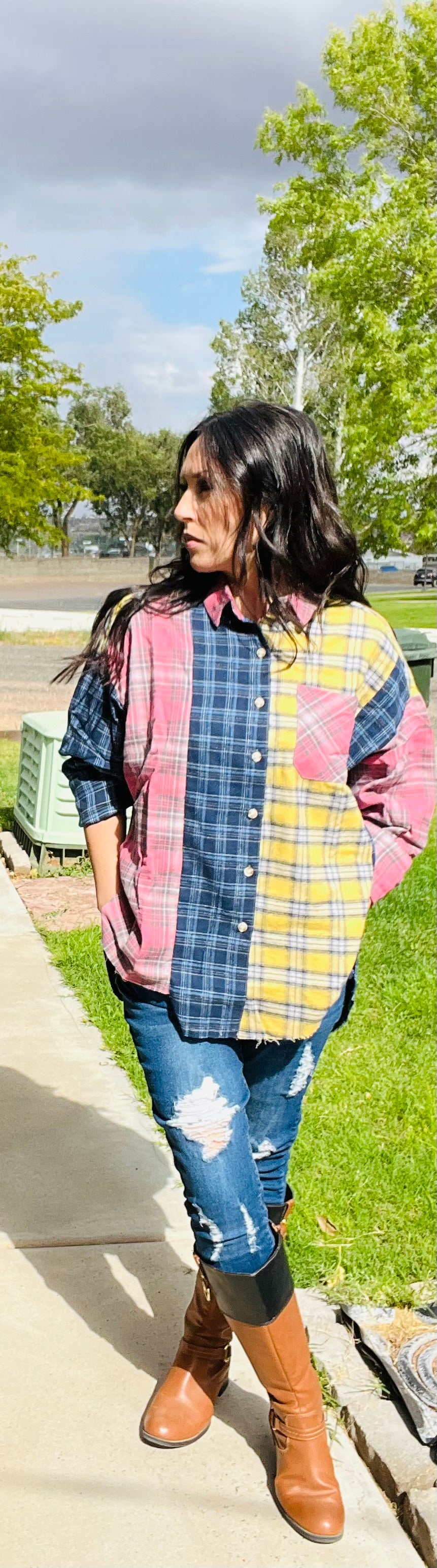 Person wearing a colorful plaid shirt and jeans standing outdoors on a sidewalk.