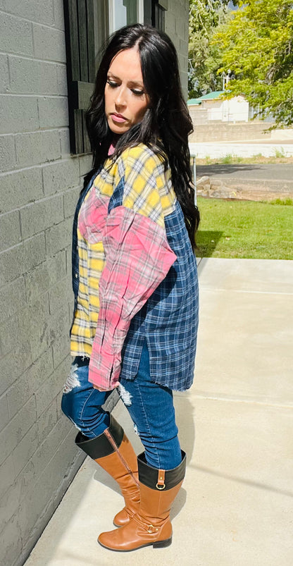 Woman wearing a plaid shirt, blue jeans, and brown boots against a gray wall.
