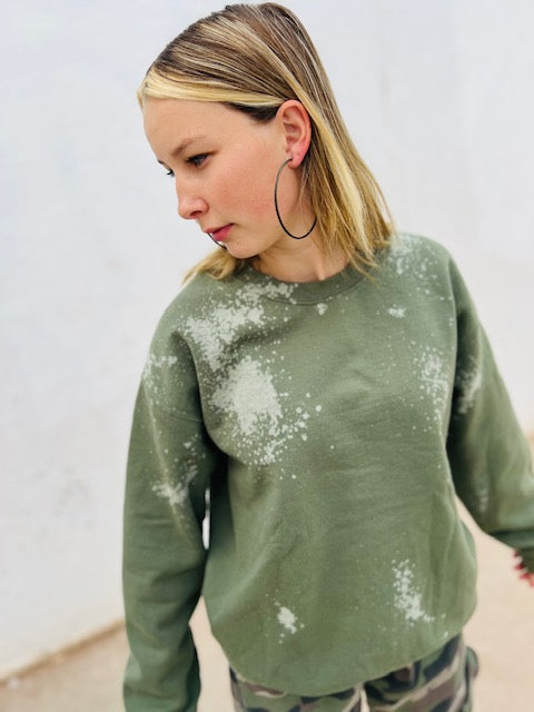 Woman wearing a green sweater with white splatter pattern against a plain background