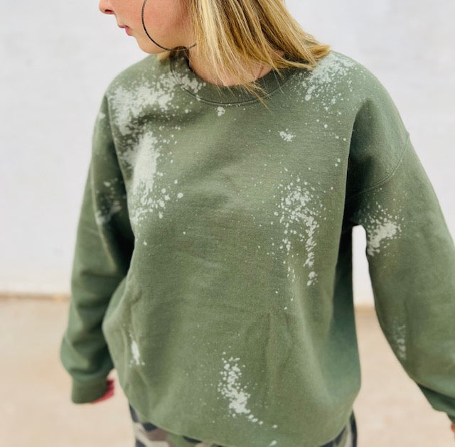 Person wearing a green sweatshirt with white splatter patterns on a neutral background