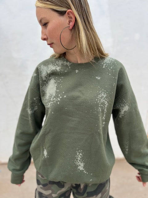 Person wearing a green sweatshirt with white splatter design against a neutral background