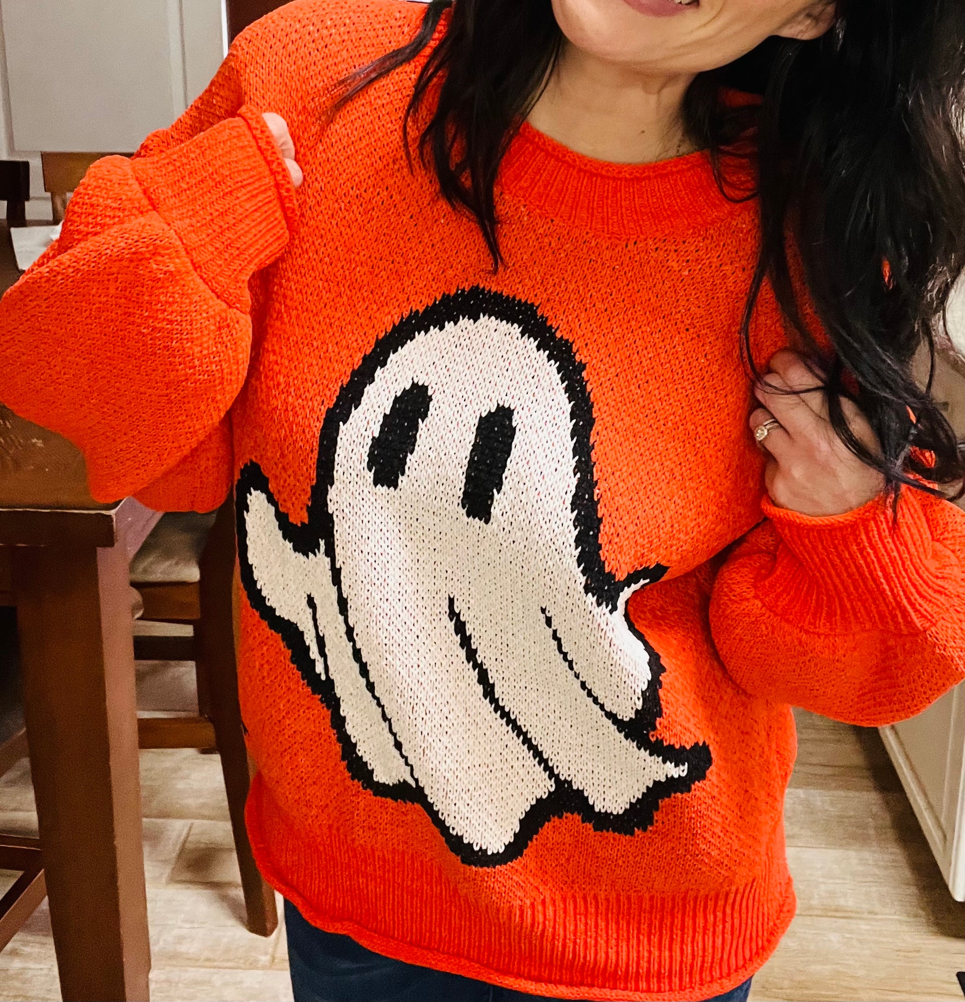 Person wearing an orange sweater with a ghost design indoors.