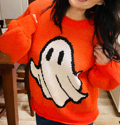 Person wearing an orange sweater with a ghost design indoors.