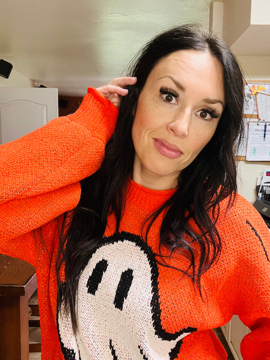 Person wearing an orange sweater with a ghost design indoors.