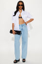 Woman wearing a white shirt, black bra, light blue jeans, and black sandals on a white background