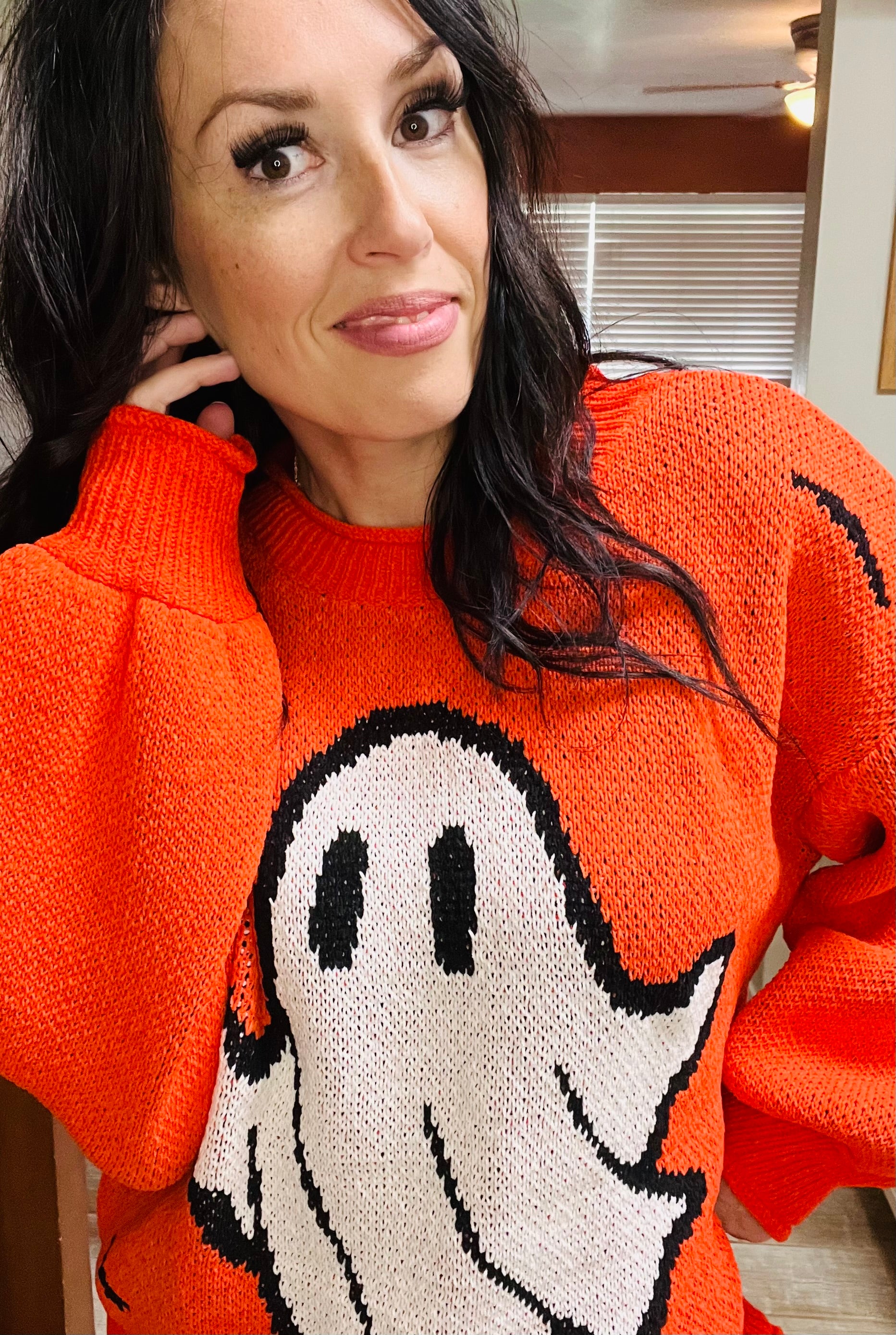 Person wearing an orange sweater with a ghost design indoors.