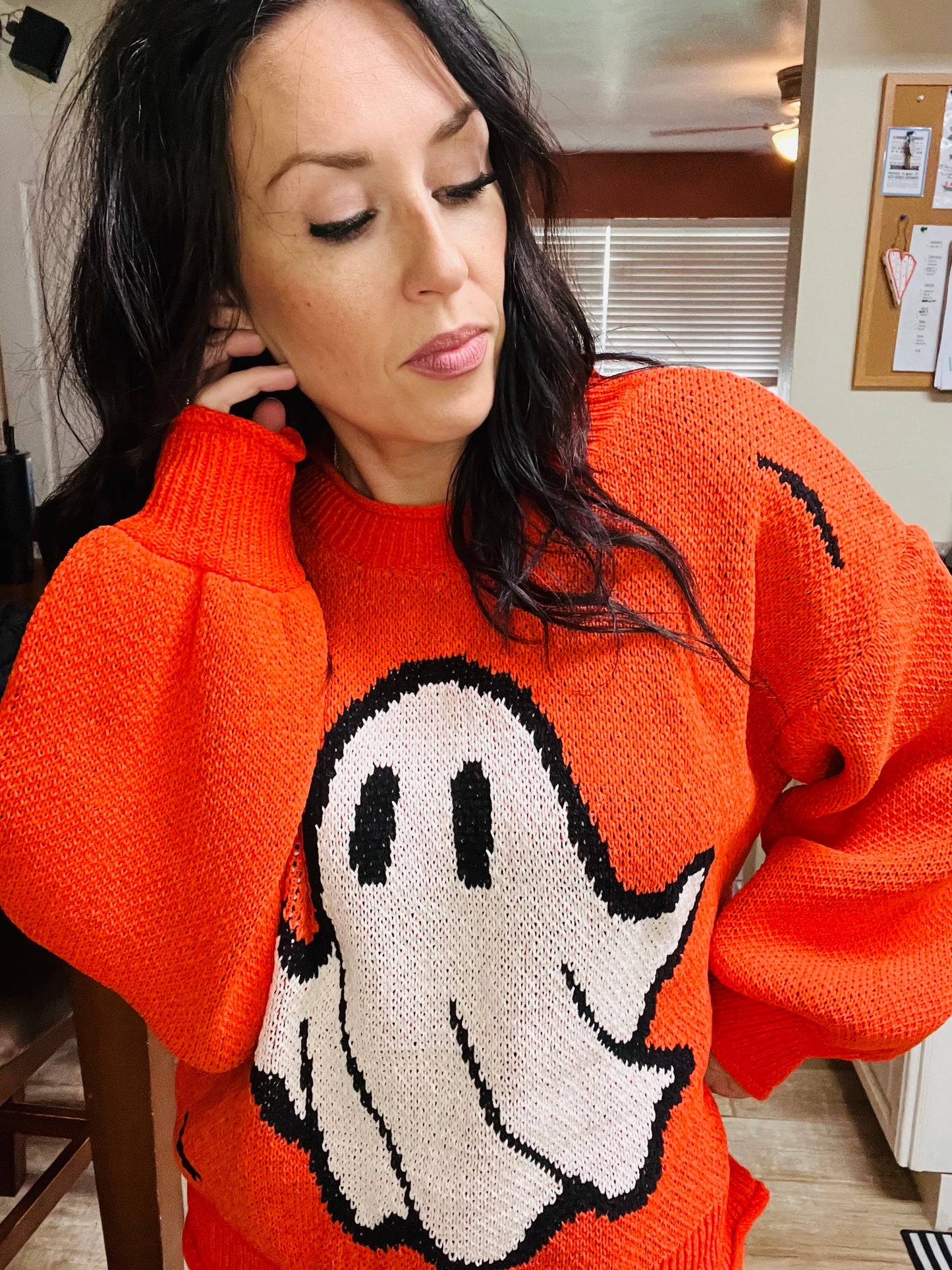 Person wearing an orange sweater with a ghost design indoors.