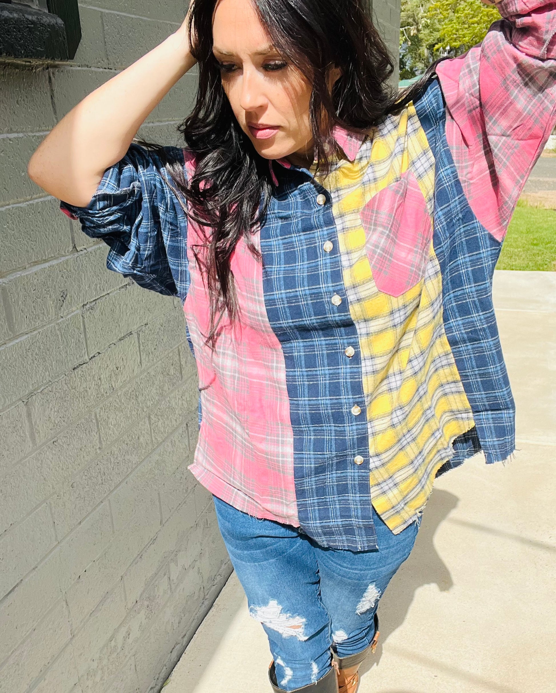 Person wearing a colorful patchwork shirt and jeans against a brick wall.