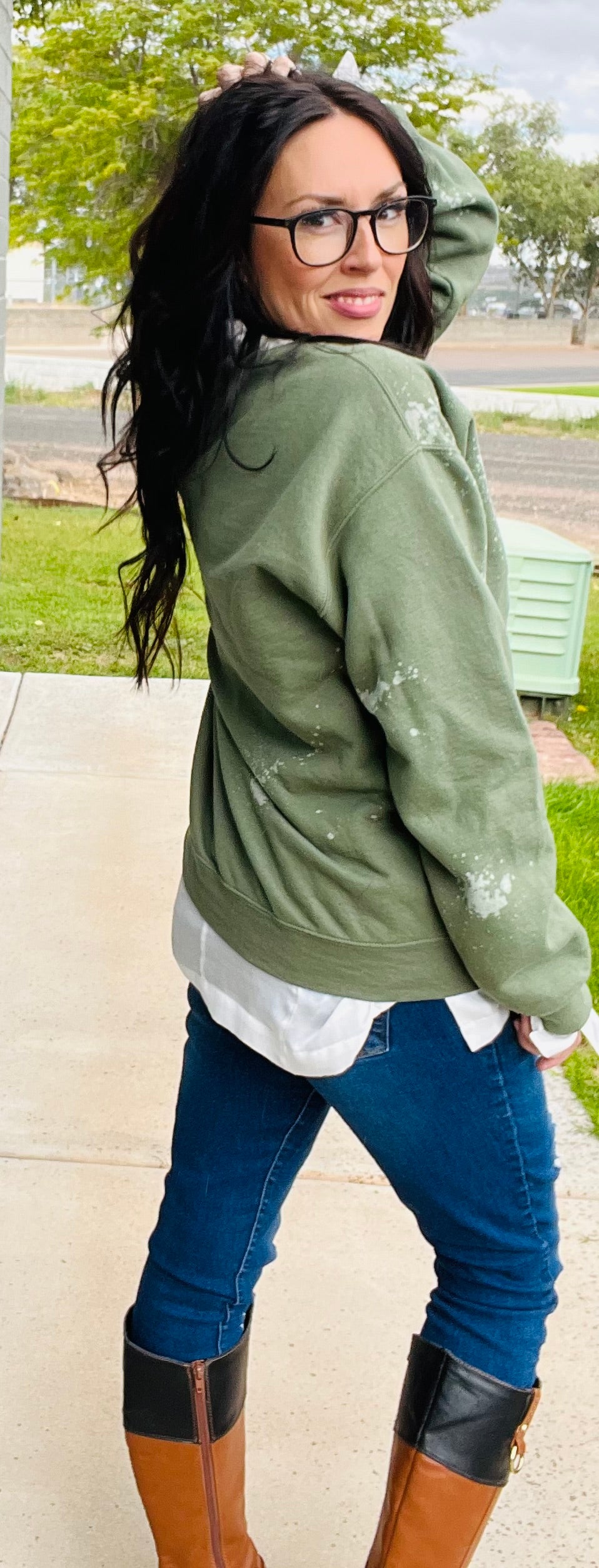 Woman wearing a green sweater, white shirt, blue jeans, and brown boots outdoors.