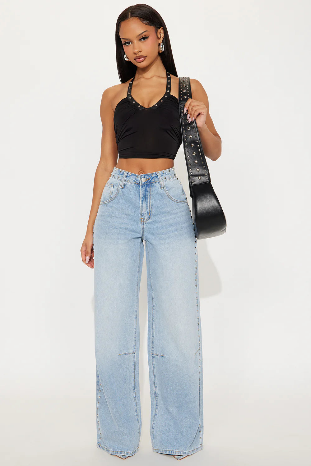 Woman wearing a black top and light blue jeans holding a black handbag on a white background