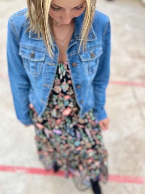 Person wearing a floral dress and blue denim jacket on a light background