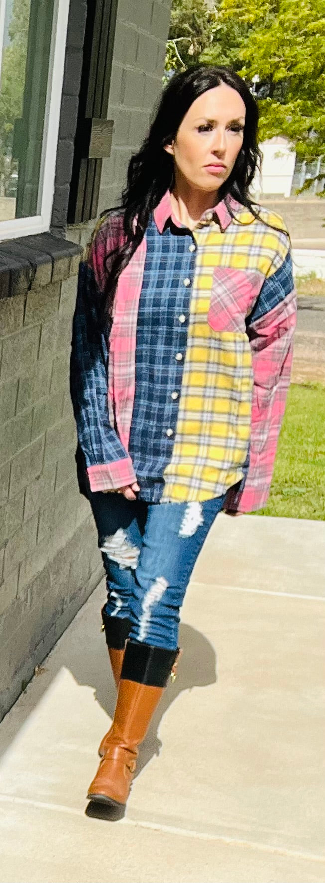 Person wearing a colorful plaid shirt and jeans on a sidewalk.