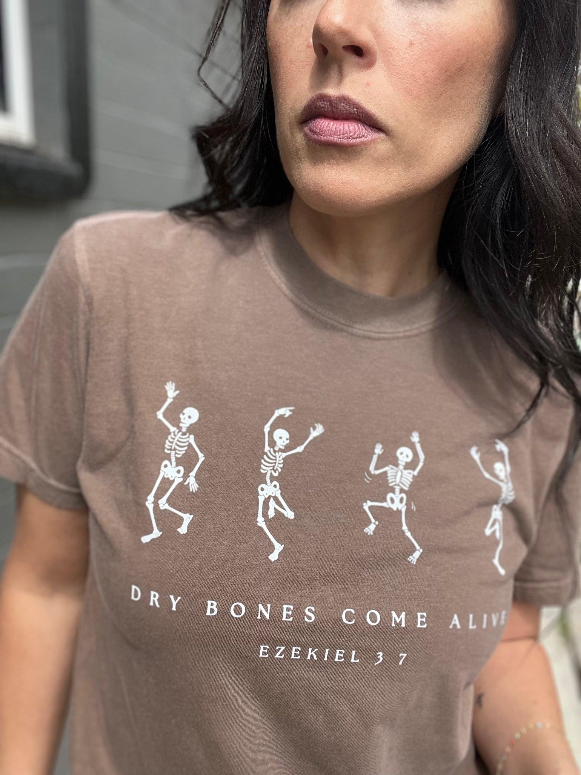 Person wearing a brown t-shirt with skeleton designs and text.
