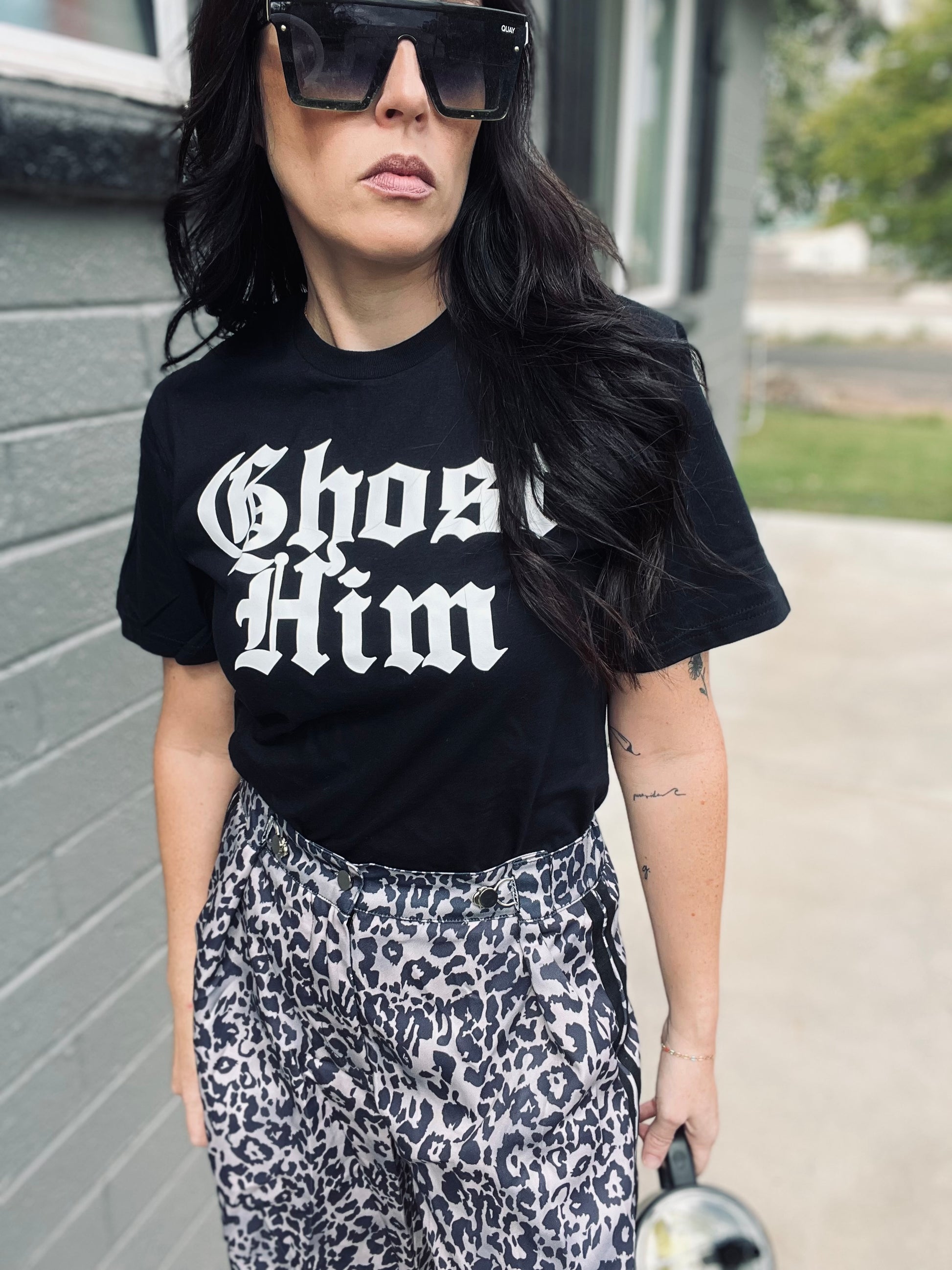 Person wearing a black t-shirt with 'Ghost Him' text and leopard print pants.