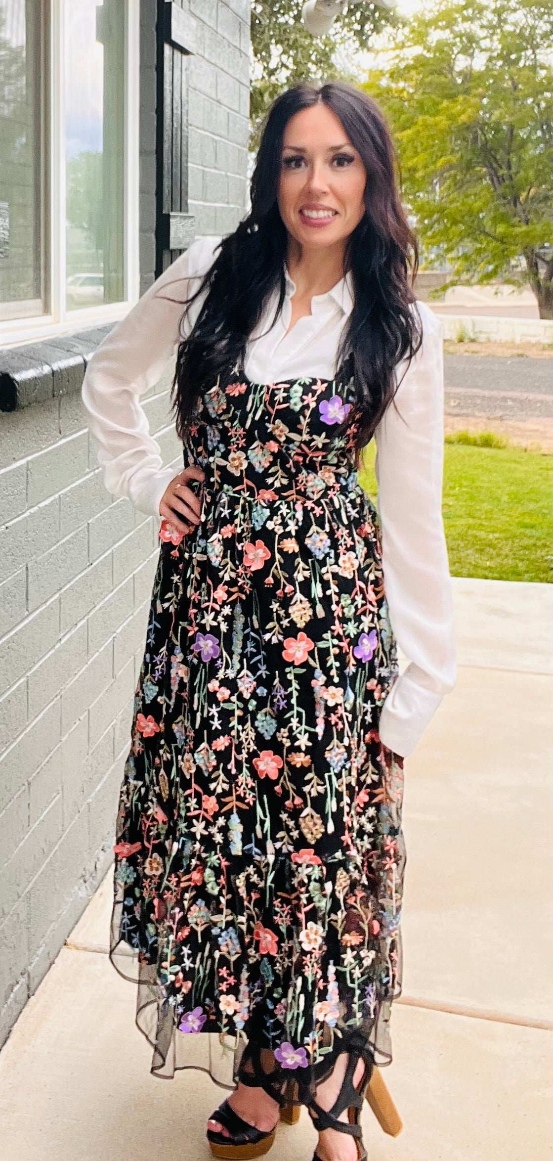 Woman wearing a floral dress and white shirt outdoors.